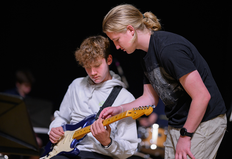 Student playing guitar with instructor