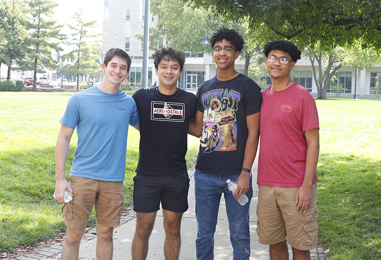 four male students in various colorful outfits, all with dark hair, two with glasses.